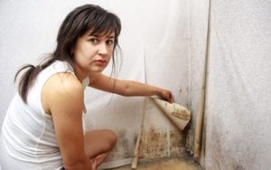 Woman peeling wallpaper to reveal black mold